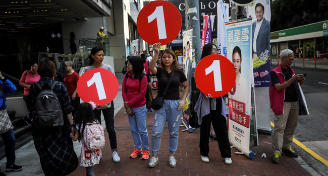 This file photo taken on November 24, 2019 shows political campaigners holding up signs to arriving voters during the district council elections in North Point in Hong Kong.  VIVEK PRAKASH / AFP