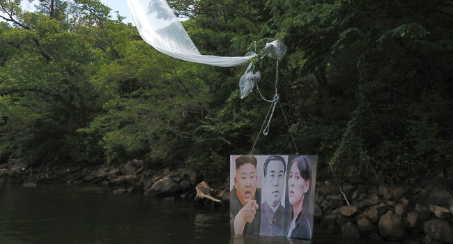 A balloon carrying a banner with portraits of North Korean leader Kim Jong Un (L), the late leader Kim Il Sung (C) and Kim Yo Jong, sister of Kim Jong Un, is caught on a tree after being launched by activists in Hongcheon on June 23, 2020. STR / YONHAP / AFP