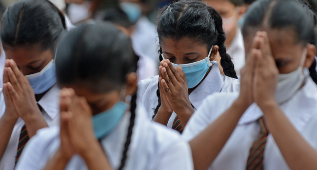 Students wearing facemasks gesture as they pray inside their school after it was reopened in Colombo on July 6, 2020. LAKRUWAN WANNIARACHCHI / AFP