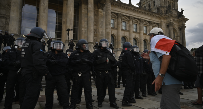 A man wrapped in a black-white-red flag leans towards the German riot policemen standing guard in front of the Reichstag building, which houses the Bundestag lower house of parliament, as protesters tried to storm in at the end of a demonstration called by far-right and COVID-19 deniers to protest against restrictions related to the new coronavirus pandemic, in Berlin, on August 29, 2020. John MACDOUGALL / AFP