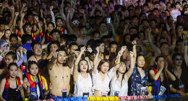 This file photo taken on August 15, 2020 shows people watching a performance as they cool off in a swimming pool in Wuhan in China's central Hubei province. STR / AFP