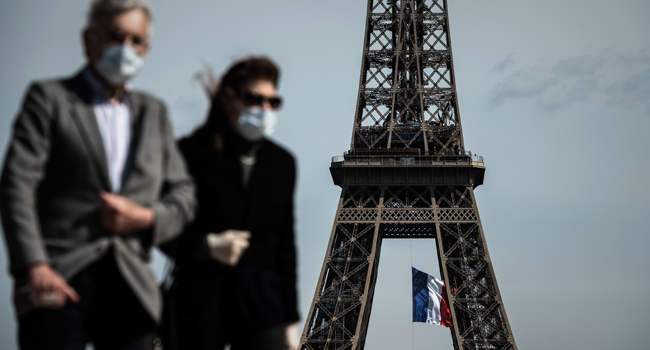 In this file photo taken on May 11, 2020, a man and a woman wearing face masks walk on Trocadero Plaza as a French national flag flies on the Eiffel Tower in background in Paris on the first day of France's easing of lockdown measures in place for 55 days to curb the spread of the COVID-19 pandemic, caused by the novel coronavirus. PHILIPPE LOPEZ / AFP