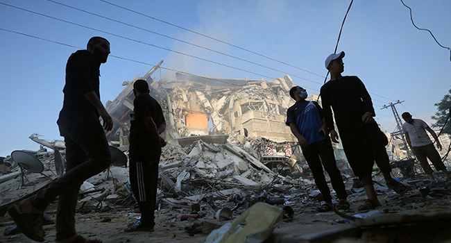 Palestinian men stand amidst debris near the al-Sharouk tower, which housed the bureau of the Al-Aqsa television channel in the Hamas-controlled Gaza Strip, after it was destroyed by an Israeli air strike, in Gaza City, on May 13, 2021.  MOHAMMED ABED / AFP