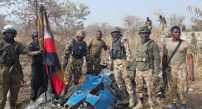 This photo, released by the Nigerian Army on March 26, 2022, shows troops standing beside what the army says are ruins of crashed Alpha Jet aircraft (NAF475).