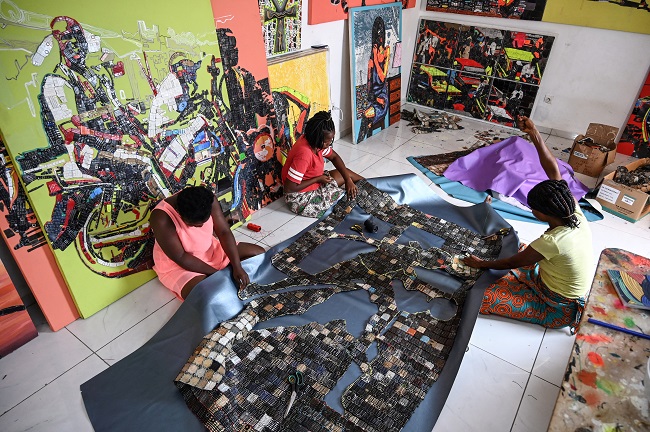 Workers of the Ivorian artist Mounou Désiré Koffi (not seen) fix the reproduced image on a carpet, one of the stages in the making of artworks with used telephone keyboards in Bingerville, a commune of Abidjan, on April 28, 2022.  (Photo by Sia KAMBOU / AFP