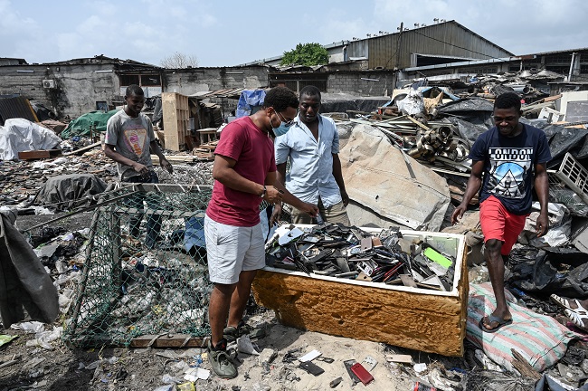 The Ivorian artist Mounou Désiré Koffi (C) looks for used telephone keyboards he uses for making artworks in Koumassi, a district of Abidjan, on December 19, 2021. (Photo by Sia KAMBOU / AFP)