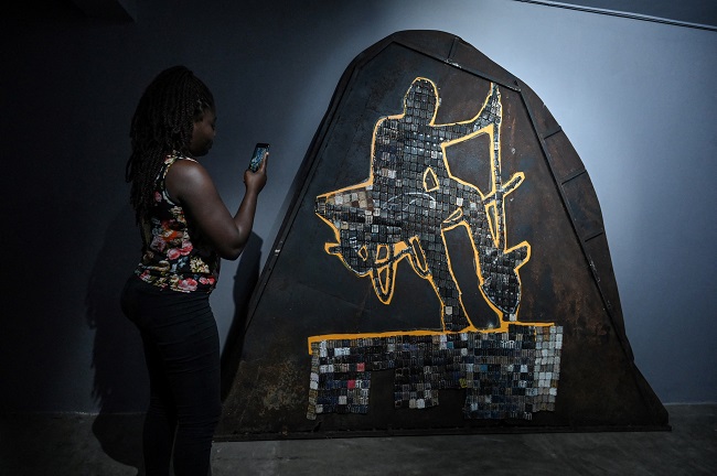 A woman films an artwork by Ivorian artist Mounou Désiré Koffi during his exhibition opening at the Donwahi foundation in Abidjan on April 29, 2022. (Photo by Sia KAMBOU / AFP)