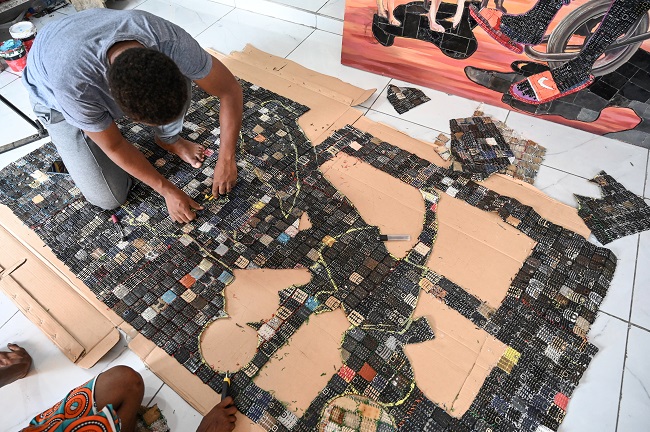 Ivorian artist Mounou Désiré Koffi cuts out an image on the screen of his artwork reproduced on a carpet of used telephone keyboards in Bingerville, a commune of Abidjan, on April 28, 2022.  (Photo by Sia KAMBOU / AFP